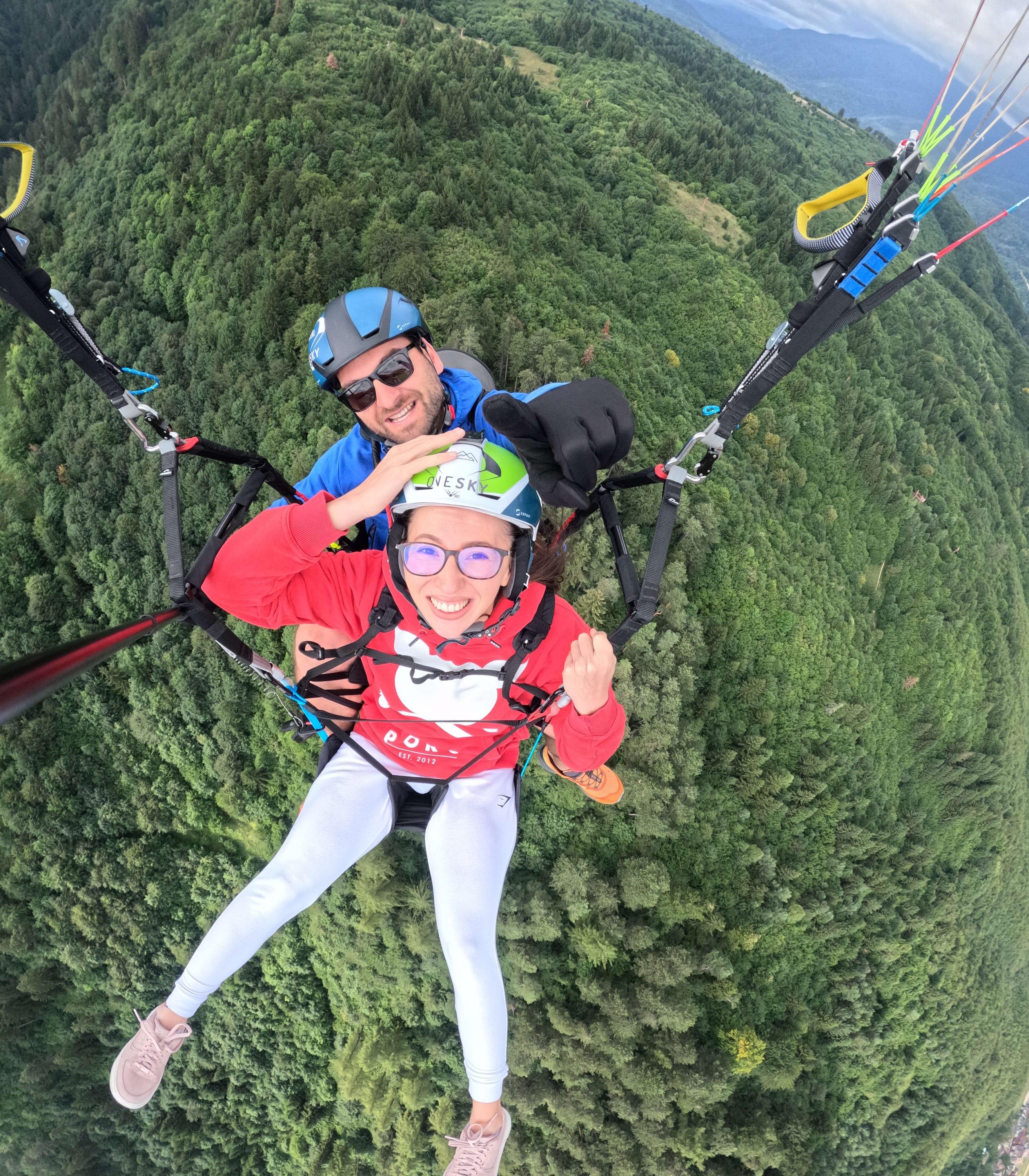 Pasageră zâmbind alături de pilot, în zbor tandem deasupra pădurii verzi
