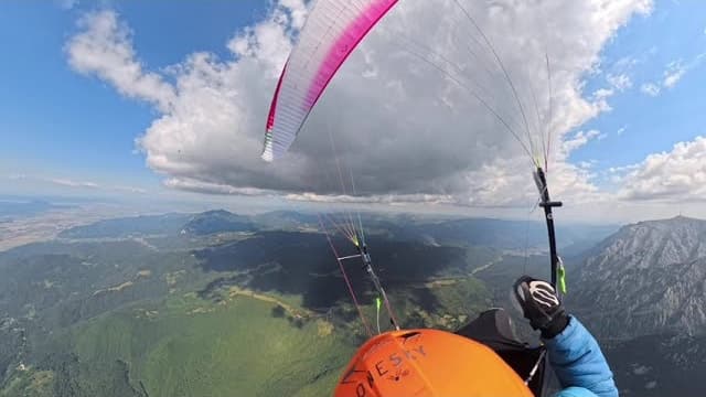 The pilot's view in flight, under a white and pink wing, above forests and rocky ridges