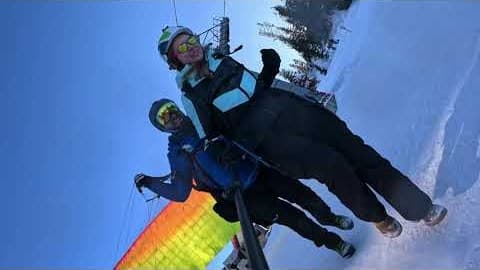 Pilot and passenger taking off from a snowy ski slope, with the yellow-orange wing