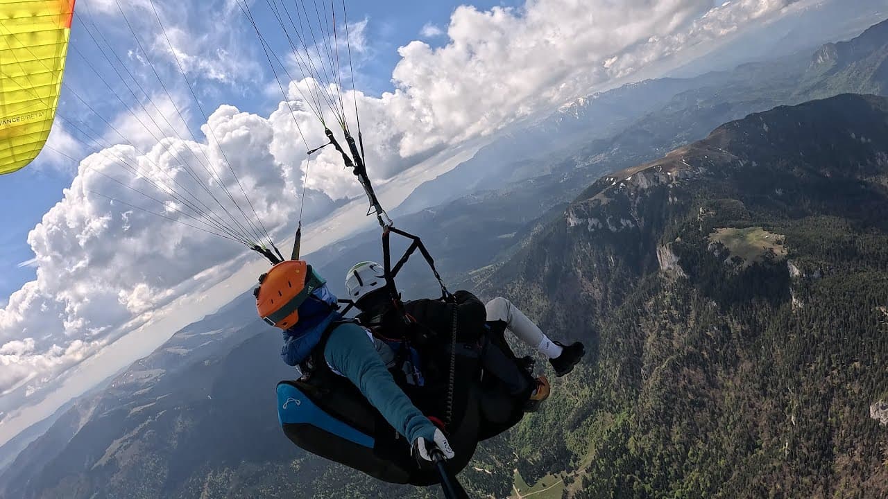 Tandem flight above forested mountains, with big summer clouds on the horizon
